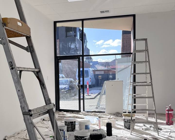 A large new window on a construction fit-out, surrounded by ladders, paint tins and drop sheets, ready for a post-build clean.