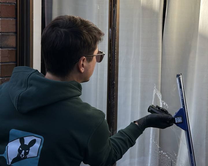 A Shiny Window cleaner squeegeeing soapy water off a home window.