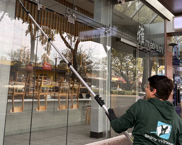 Close-up of a Shiny Window cleaner working a water-fed pole across shopfront glass.